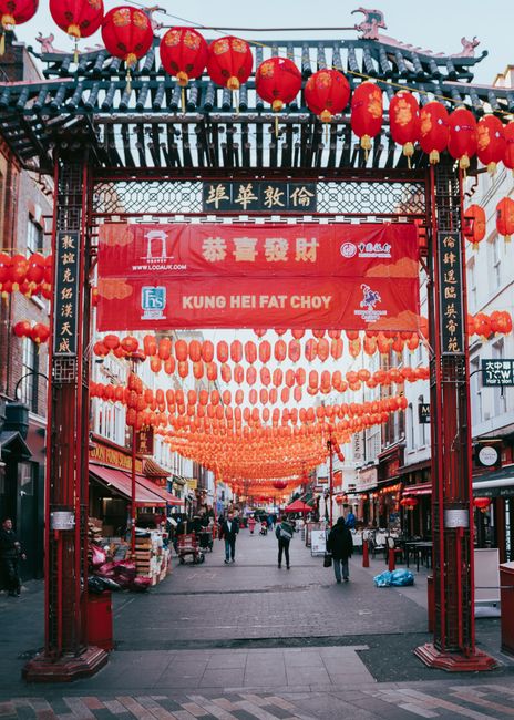 A vibrant street scene in Gerrard Street Chinatown London decorated for a festive celebration, featuring a traditional red archway adorned with intricate black and gold Chinese characters at the top.